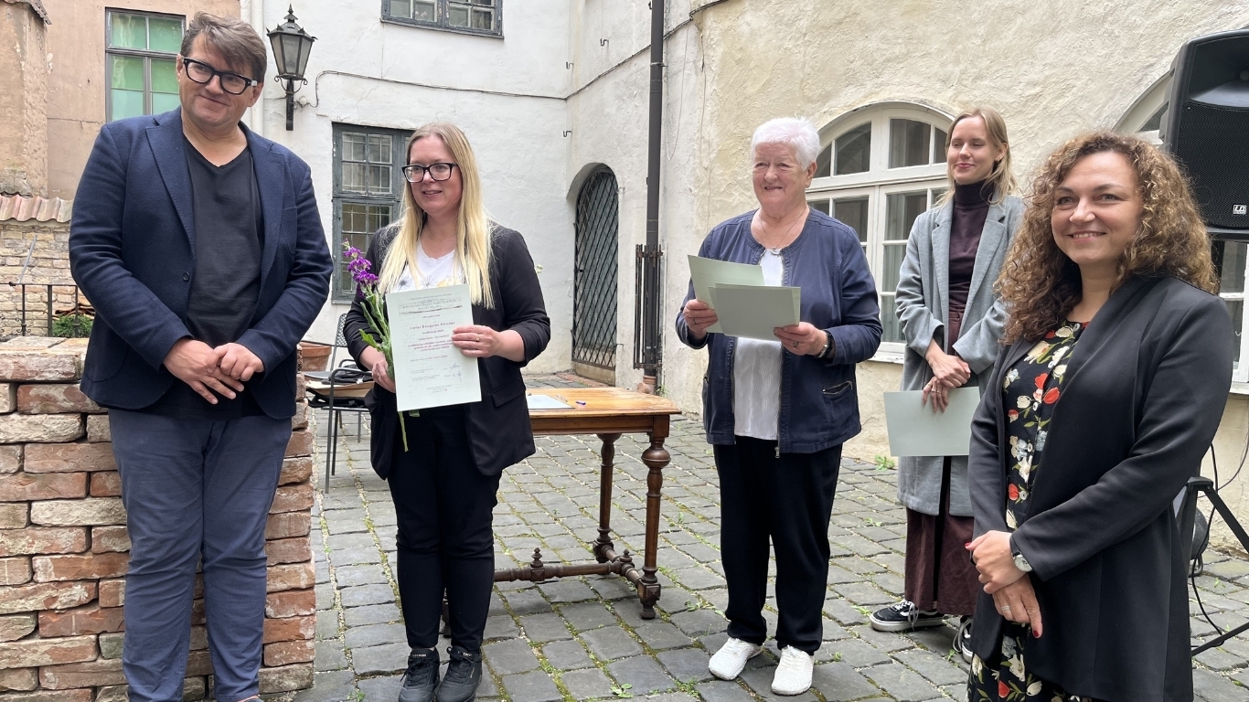 Smaidīga cilvēku grupa pozē attēlam. Viena no sievietēm attēlā saņēmusi diplomu.