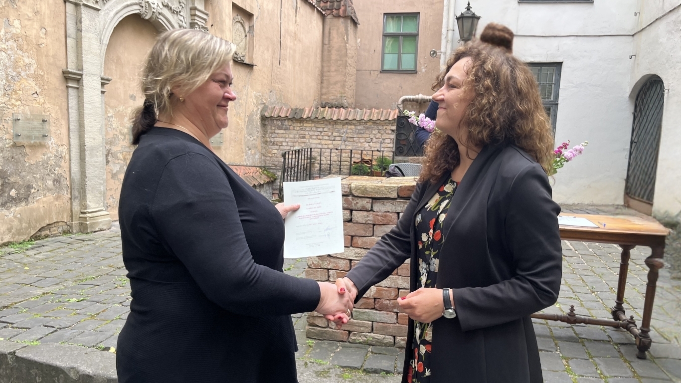 Sieviete sniedz otrai sievietei diplomu.