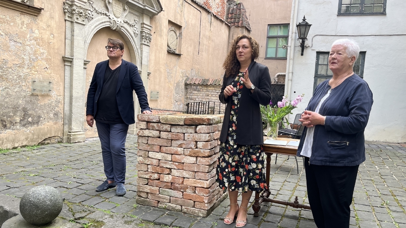 Trīs cilvēki vēsturiskā vidē stāv un uzrunā kadrā neredzamu publiku.