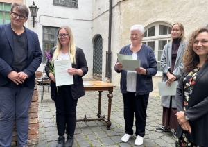 Smaidīga cilvēku grupa pozē attēlam. Viena no sievietēm attēlā saņēmusi diplomu.