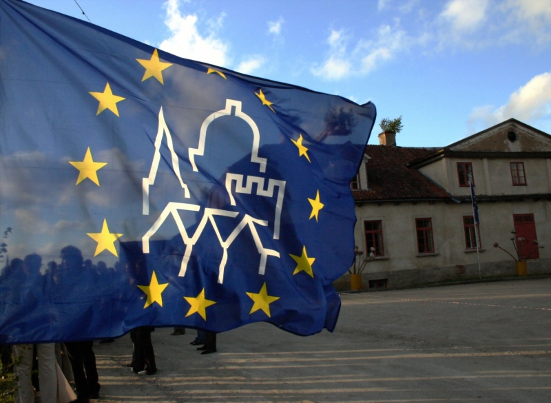 Plīvojošs EKMD karogs, fonā sena ēka