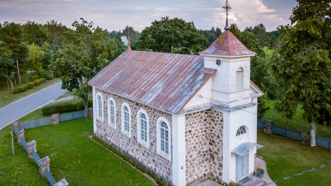 Aero foto redzama neliela, gaiša baznīca vasarīgā ainā. Mūrēta no akmens, apmestās fasādes daļas ap logiem, durvīm un nelielu tornīti, kas knapi paceļas virs divslīpju jumta kores, ir baltas. Tornīša galā - krusts. Rūsējis skārda jumts, sīkrūtiņu logi ar aploci. Baznīca ir  centrā. Labā apakšējā stūrī stiepjas celiņš, apkārt zālājs, ko ieskauj žogs, tā raksturs nav nolasāms. Kreisajā pusē asfaltēts ceļš. Debesis ir vasarīgi zilas ar mākoņiem un fonā uz visām pusēm redzami zaļi koki.