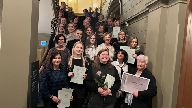 Grupas fotogrāfija uz kāpnēm, kurā redzami pasākuma dalībnieki un restauratori. Centrā, priekšplānā, redzamas sievietes ar diplomiem un viena sieviete tur Ministru kabineta Atzinības rakstu rāmītī.