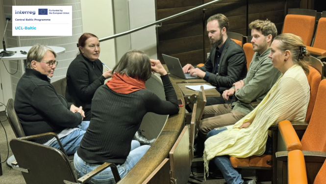 Semināra zālē seši projekta “UCL-Baltic” dalībnieki sēž ap apaļu galdu un pārrunā zemūdens kultūrvēsturisko ainavu izpētes jautājumus. Grupā ir trīs sievietes un trīs vīrieši, viens no dalībniekiem strādā pie klēpjdatora. Apkārt redzamas auditorijas rindas ar oranžiem krēsliem. Kreisajā augšējā stūrī ir projekta logo.