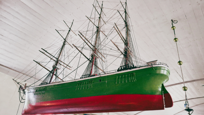 Attēls atspoguļo pie griestiem piekārtu burukuģa modeli. Griesti ir no baltiem dēļiem, bet kuģis ir zaļi sarkans. Tam ir trīs masti, buras nav uzvilktas. Kuģa modelis ir viens no Eiropas kultūras mantojuma dienu 2025 objektiem.