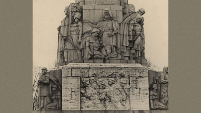 Attēlā uz pelēcīga fona redzama melnbalta fotogrāfija, kurā ir redzama Brīvības pieminekļa daļa, kas vērsta pret Operas pusi. Tajā izcelts cilnis, kas attēlo Bermontiādi, kas saistīts ar Brīvības cīņām un to, kāpēc svinam Lāčplēša dienu.