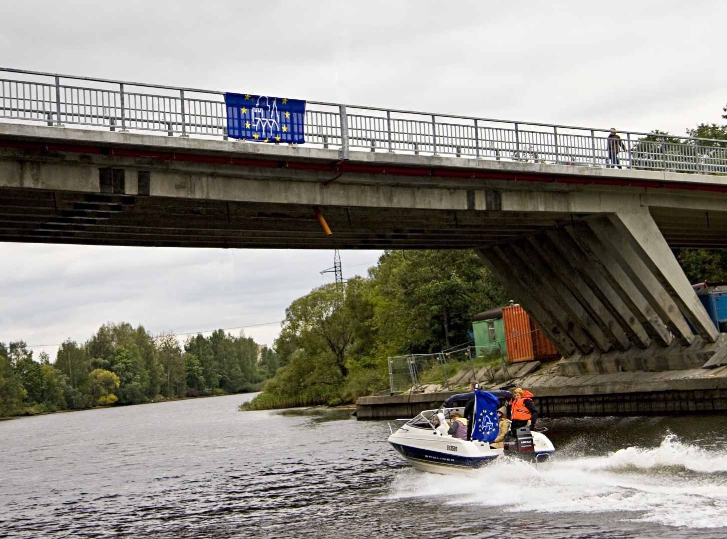 Tilts ar EKMD karogu, pa ūdeni brauc motorlaiva