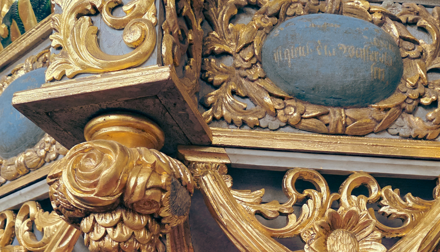 Attālā redzama daļa no lielāka kokgriezuma. Darbs ir senlaicīgs, kokgrebumi attēlo ziedus un lapas, tie ir zeltīti, fons ir tumši pelēks. Labajā pusē augšā redzams padzisis, sens uzraksts.