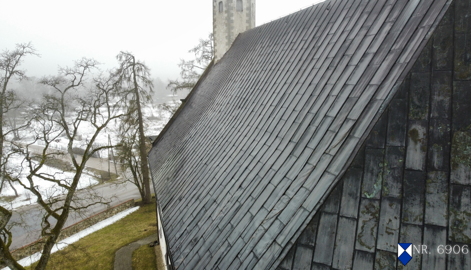  Attēlā redzams Matīšu luterāņu baznīcas pelēks, slīps jumts, kas pārklāts ar horizontālām, taisnstūrveida plāksnēm. Jumta labajā pusē ir redzama neliela, balta kvadrātveida zīme ar zilu rombu - kultūras pieminekļu aizsardzības zīme - un objekta valsts aizsardzības numurs "NR. 6906". Kreisajā pusē ir redzami koki bez lapām un tālumā – ēkas torņa augšdaļa. Zeme ir klāta ar sniega paliekām.