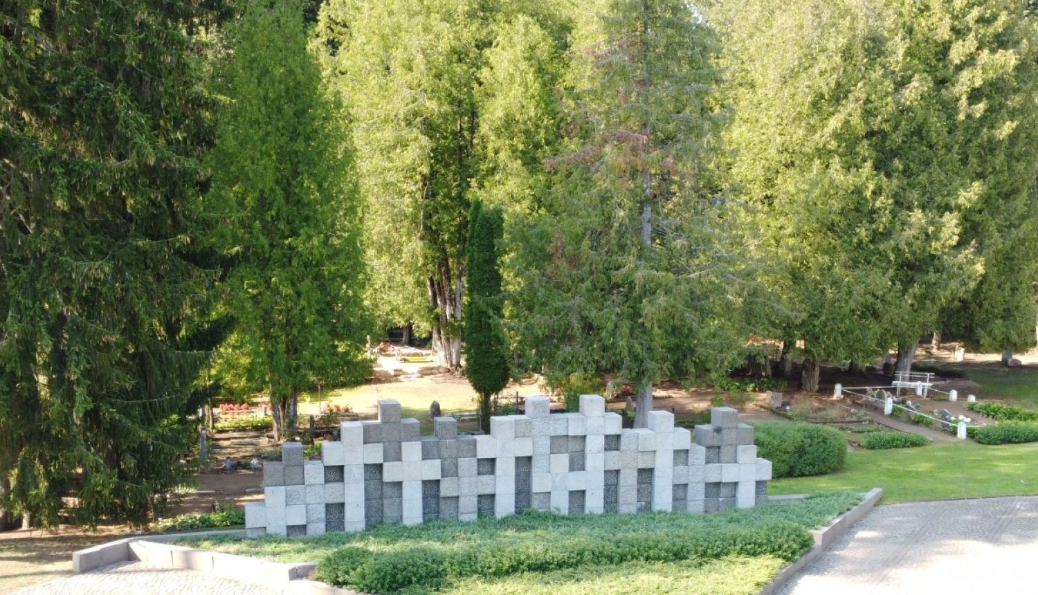 Piemiņas vieta ar kapiem, plašs lauks ar baltiem dažādu izmēru krustiem centrā. Aiz krustiem zaļo koki.