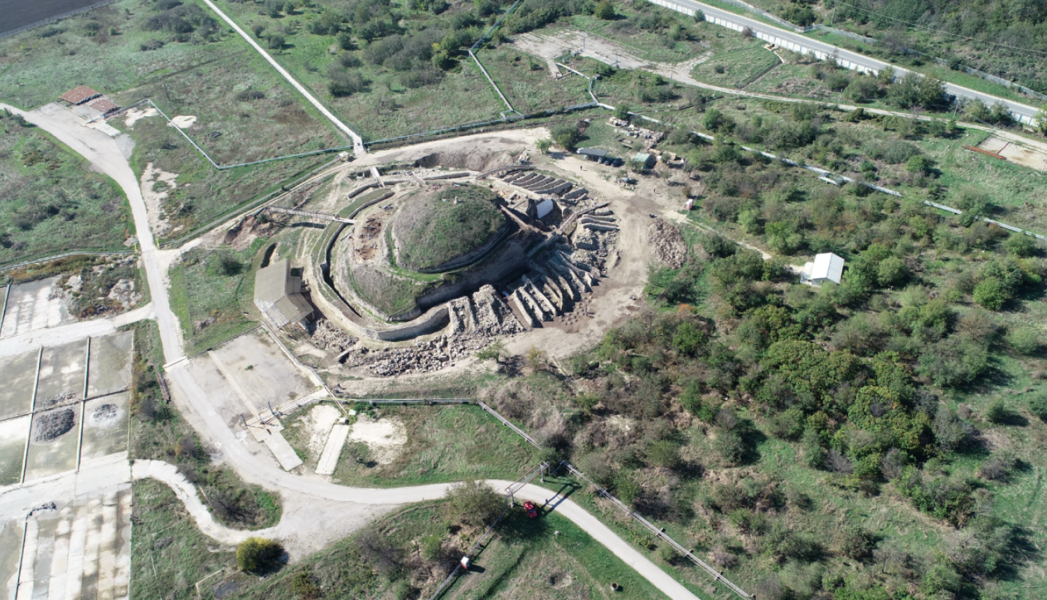 No gaisa uzņemta ainava ar zaļu vidi. To šķērso ceļi un redzami lauki. Centrā ir liels, apaļš objekts. Tam apkārt ir dažādi reljefa pārveidojumi.