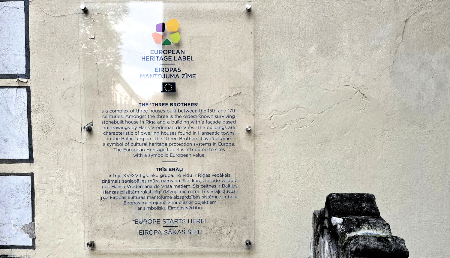 Attēlā redzama pie ēku ansambļa "Trīs brāļi" piestiprinātā Eiropas mantojuma zīme ar aprakstu. Zīme ir no stikla, lai pilnībā neaizsegtu vēsturisko ēku un būtu mazāk uztverama vidē, pati zīme ir krāsaina, bet burti - tumši zili.