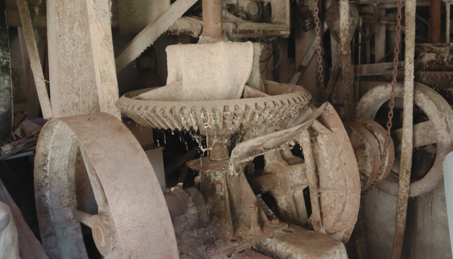 Tuvplāna attēls vecām, putekļainām un rūsas klātām ūdensdzirnavu iekārtām telpā. Centrālajā daļā dominē liels, plats metāla zobrats ar vertikālu asi, kas ir daļa no dzirnavu mehānisma. Abās pusēs redzami lieli rati. Mehānismu klāj putekļi un zirnekļu tīkli, redzams, ka tas ilgstoši nav lietots. Griesti un koka konstrukcijas ap detaļām ir klāti ar biezu gaišu kārtu. Tumšajā fonā redzamas citas iekārtu daļas un ķēdes, kas norāda uz dzirnavu telpas sarežģītību.